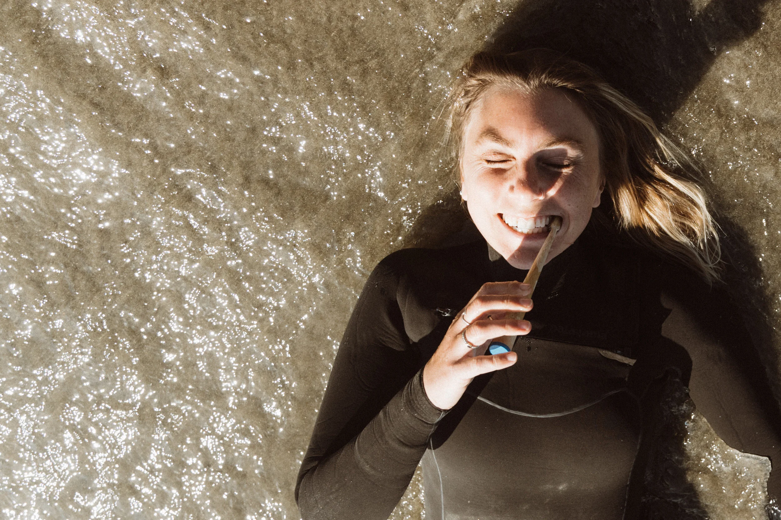 A woman in a wetsuit brushes her teeth with a MABLE eco-friendly toothbrush, promoting sustainable oral care.
