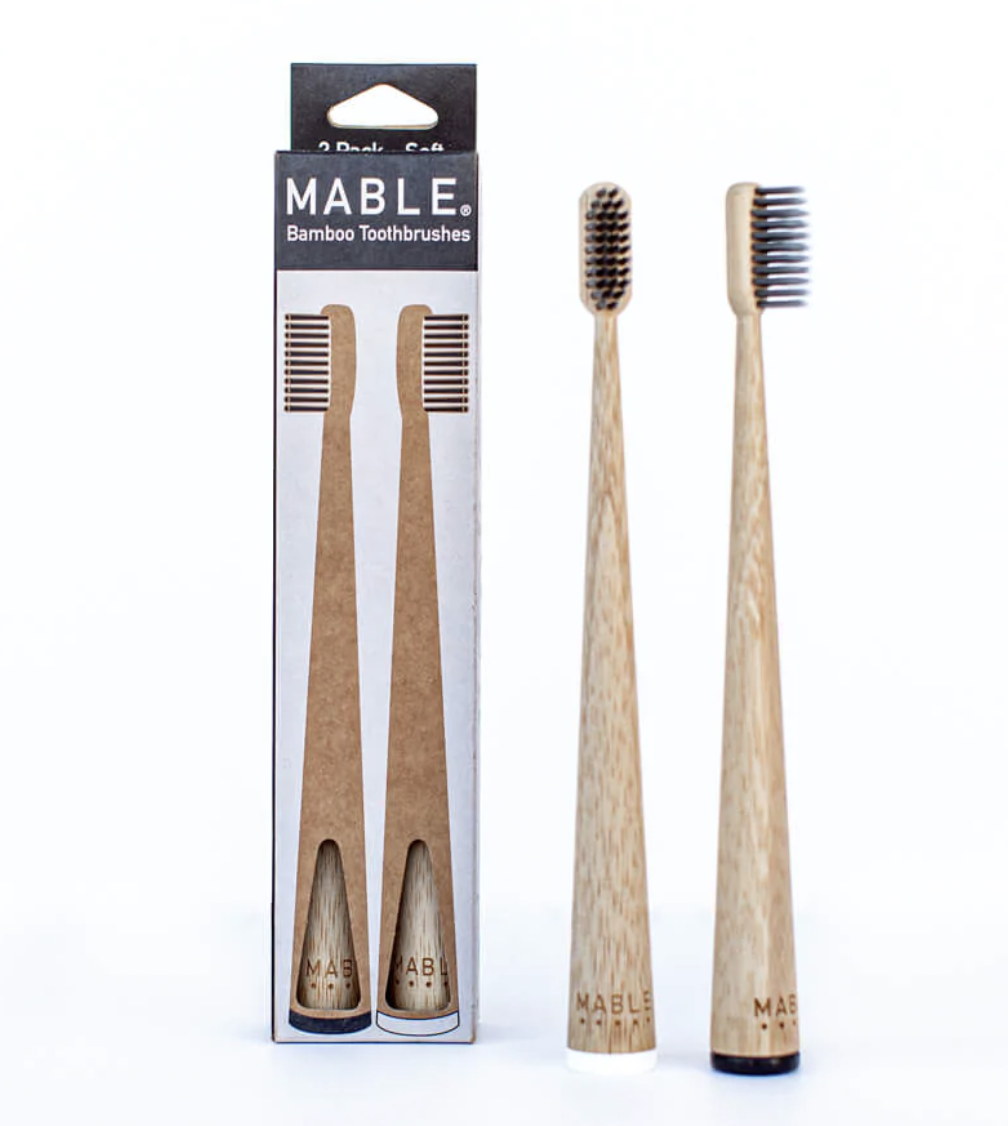 Two eco-friendly toothbrushes with wooden handles beside a cardboard box labeled "MABLE Eco-Friendly Toothbrushes."