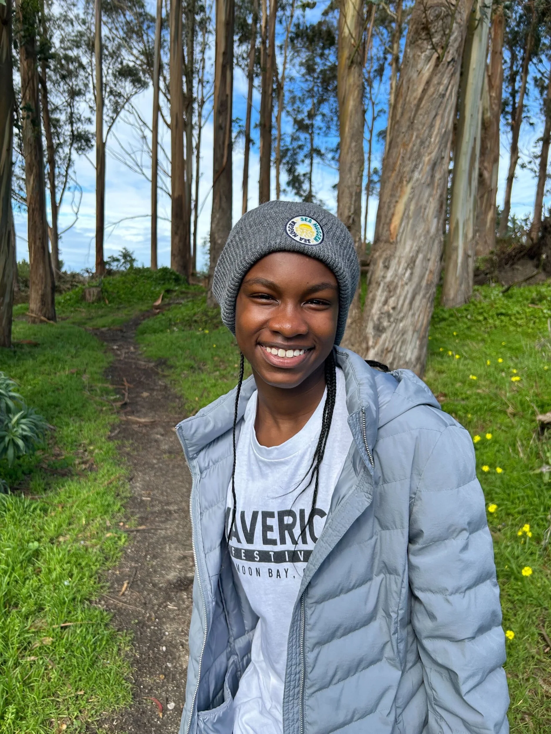 Smiling child wearing a gray Sea Hugger beanie on a forest trail, showcasing eco-friendly, sustainable winter accessories.