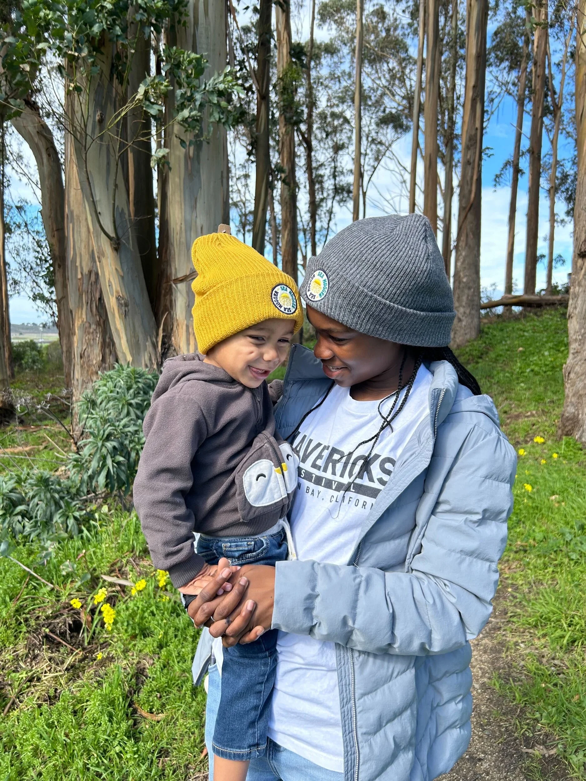 iblings wearing Sea Hugger beanies, embracing eco-friendly fashion in a natural setting, highlighting sustainable winter gear for kids and teens.