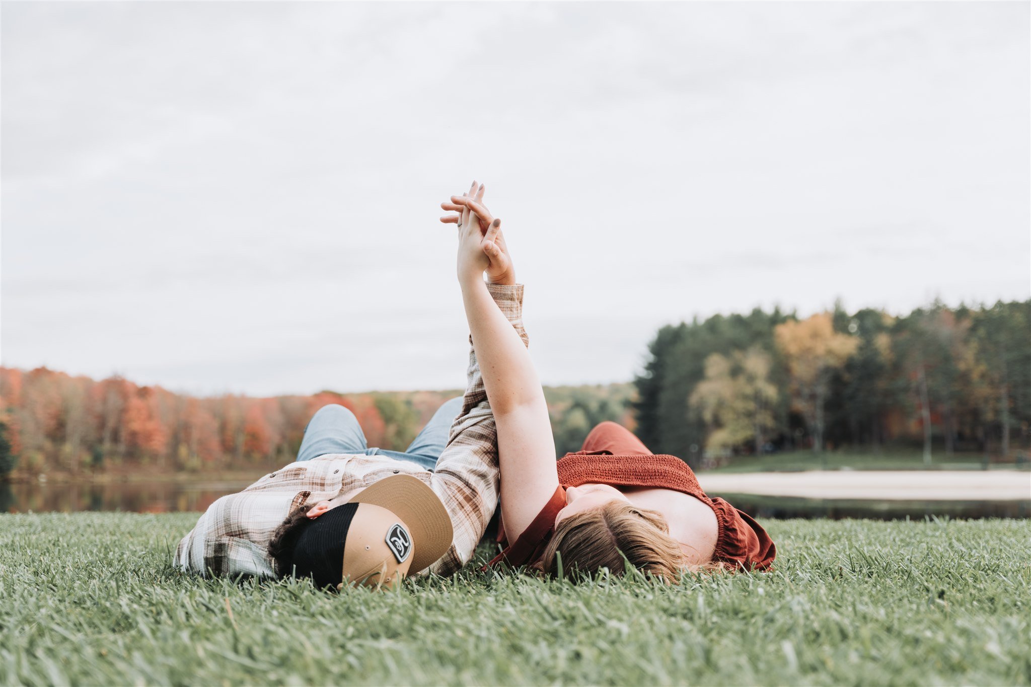 Couple holding hands while lying in the grass during their engagement session at Parker Dam, Penfield, PA.