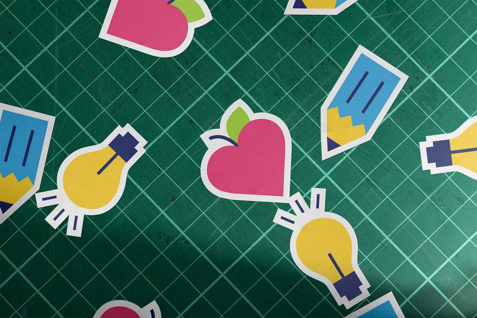 Stickers depicting pencils, heart-shaped apples, and lightbulbs are scattered on a cutting board