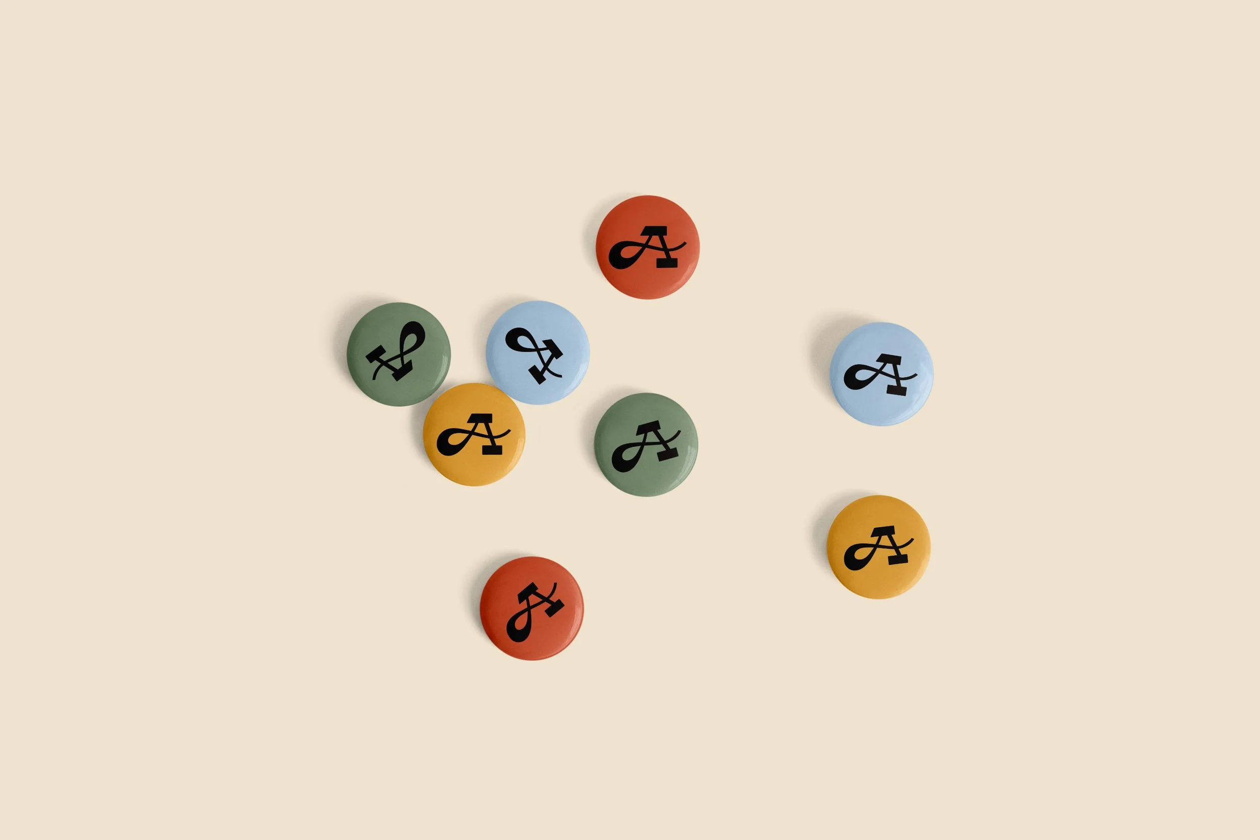 Pin buttons in various colors with a handlettered A printed on them scattered on a yellow background