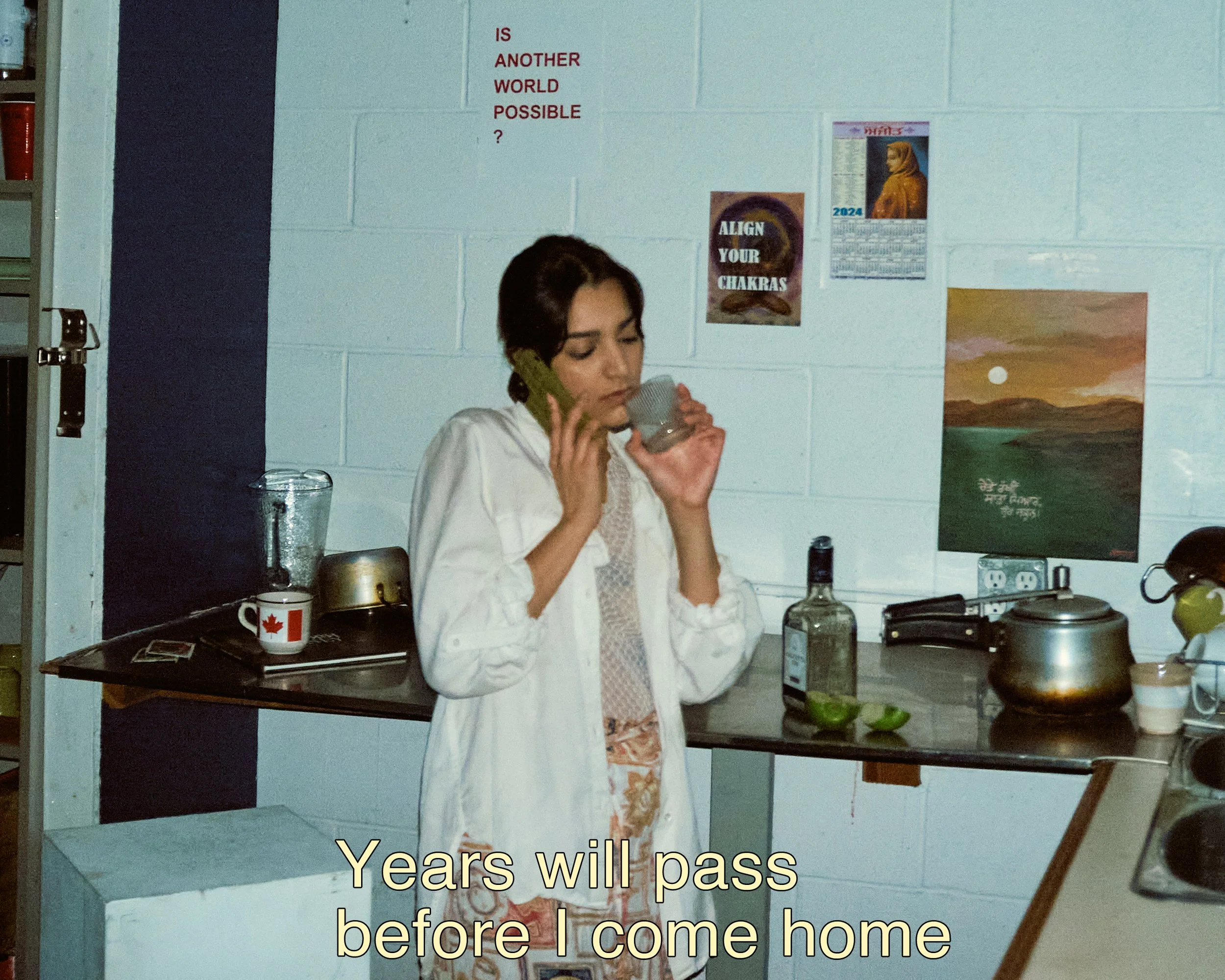 A woman standing in a kitchen, drinking from a mug, with posters on the wall behind her, and a subtitle that reads, 'Years will pass before I come home'.