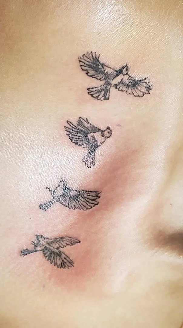 Four small flying bird tattoos in a vertical line on skin.