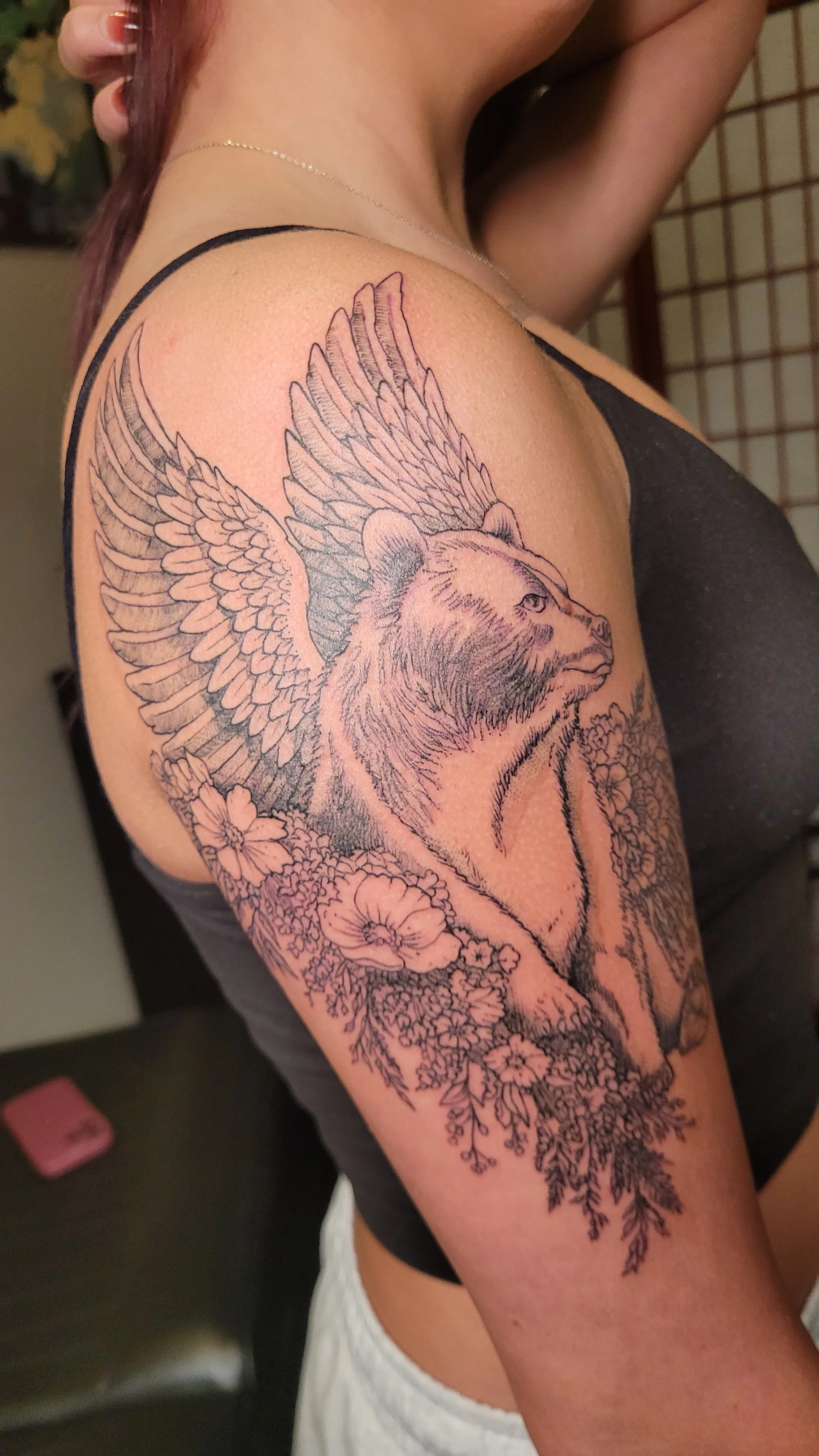 Illustrated line art tattoo bear with angel wings sitting in an arrangement of wildflowers