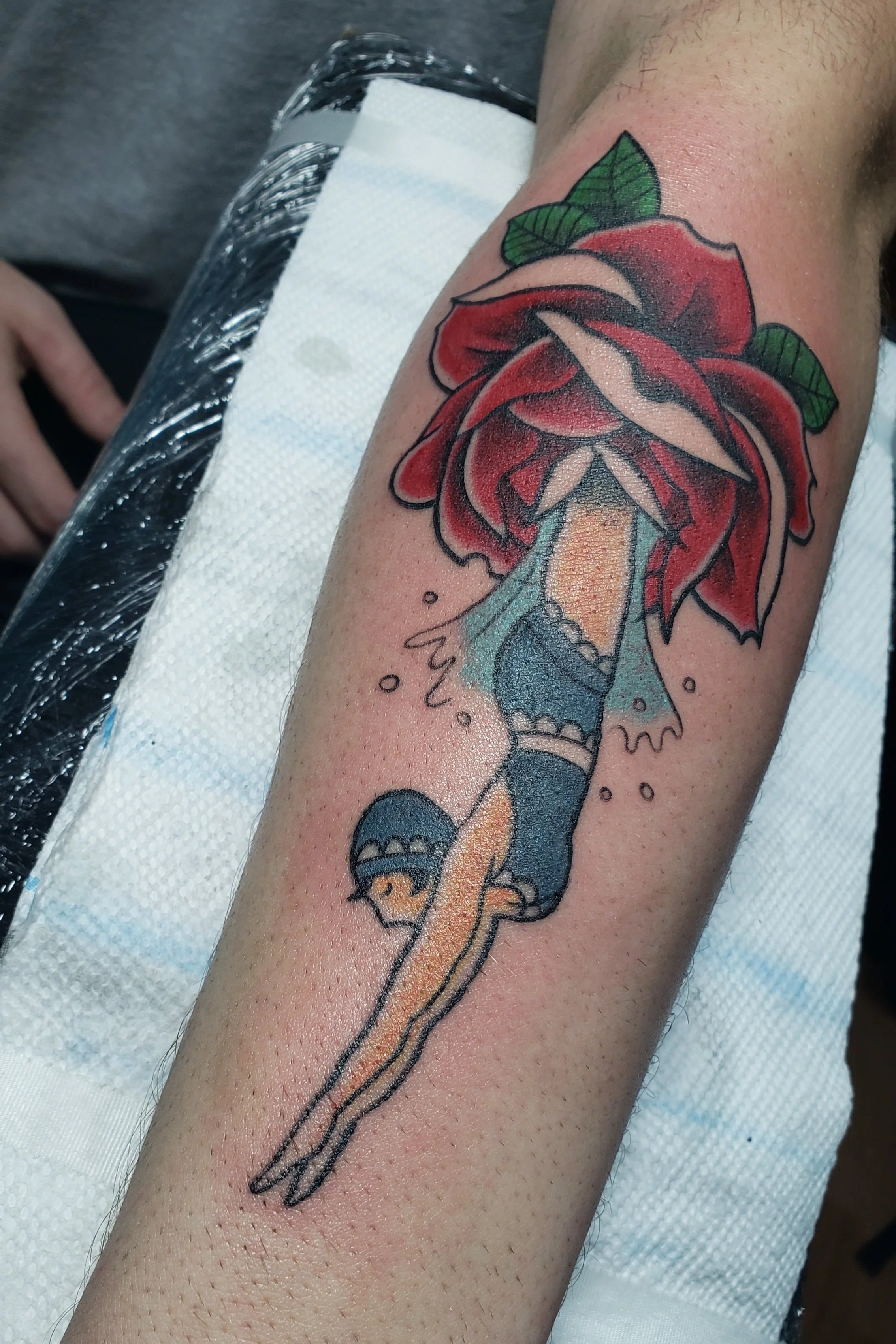 Traditional-style tattoo of red rose with a lady swimmer emerging in a dive from the center