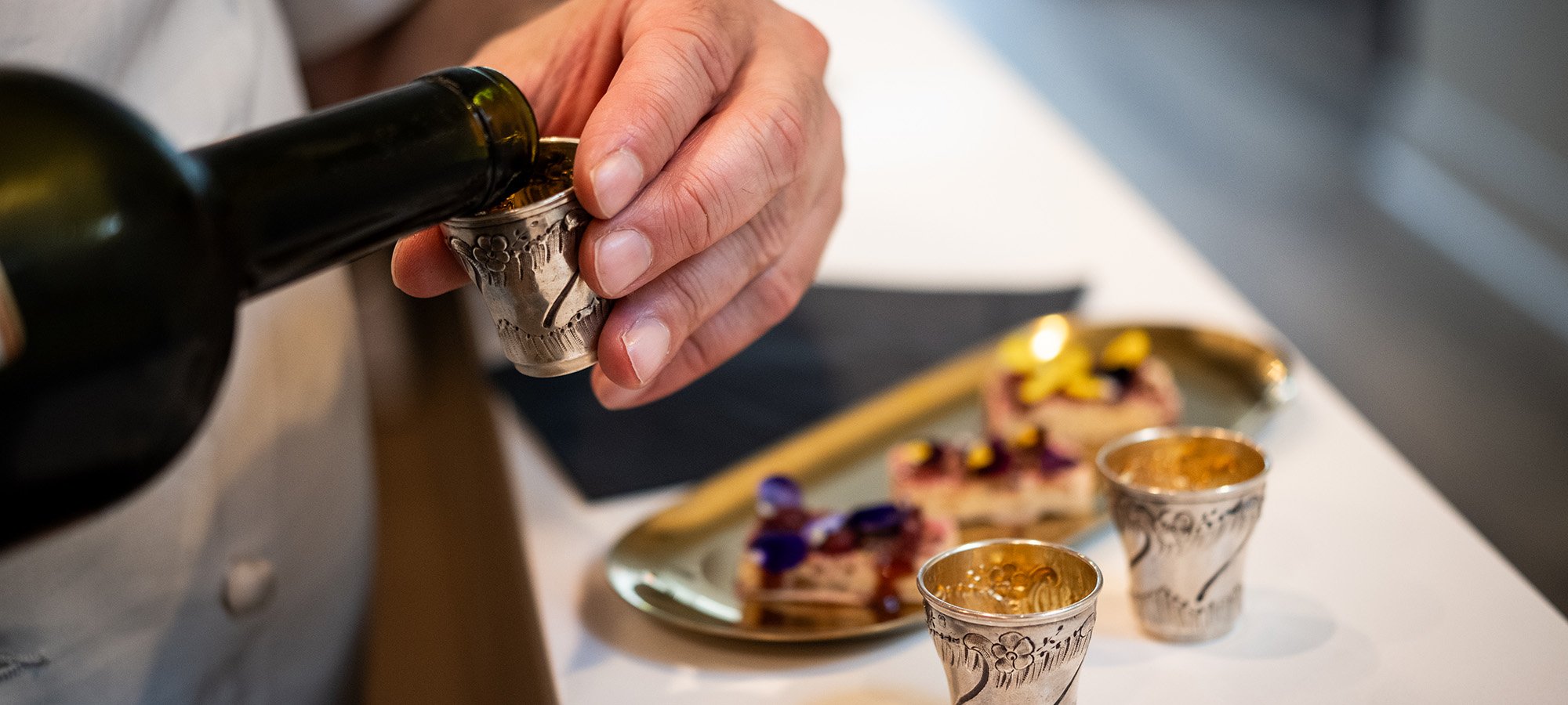 Chef Danny pouring vermouth into antique silver shot glasses for welcome bites