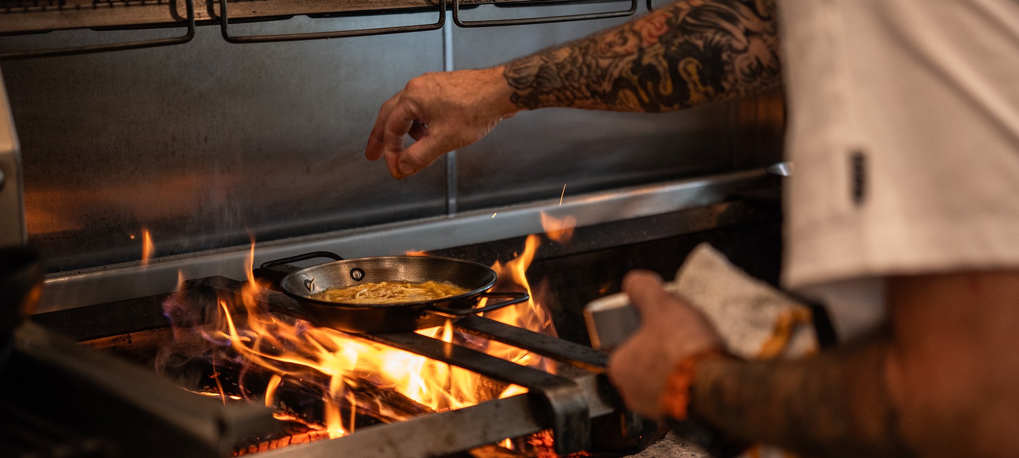 Chef sprinkling salt onto paella bubbling over open fire