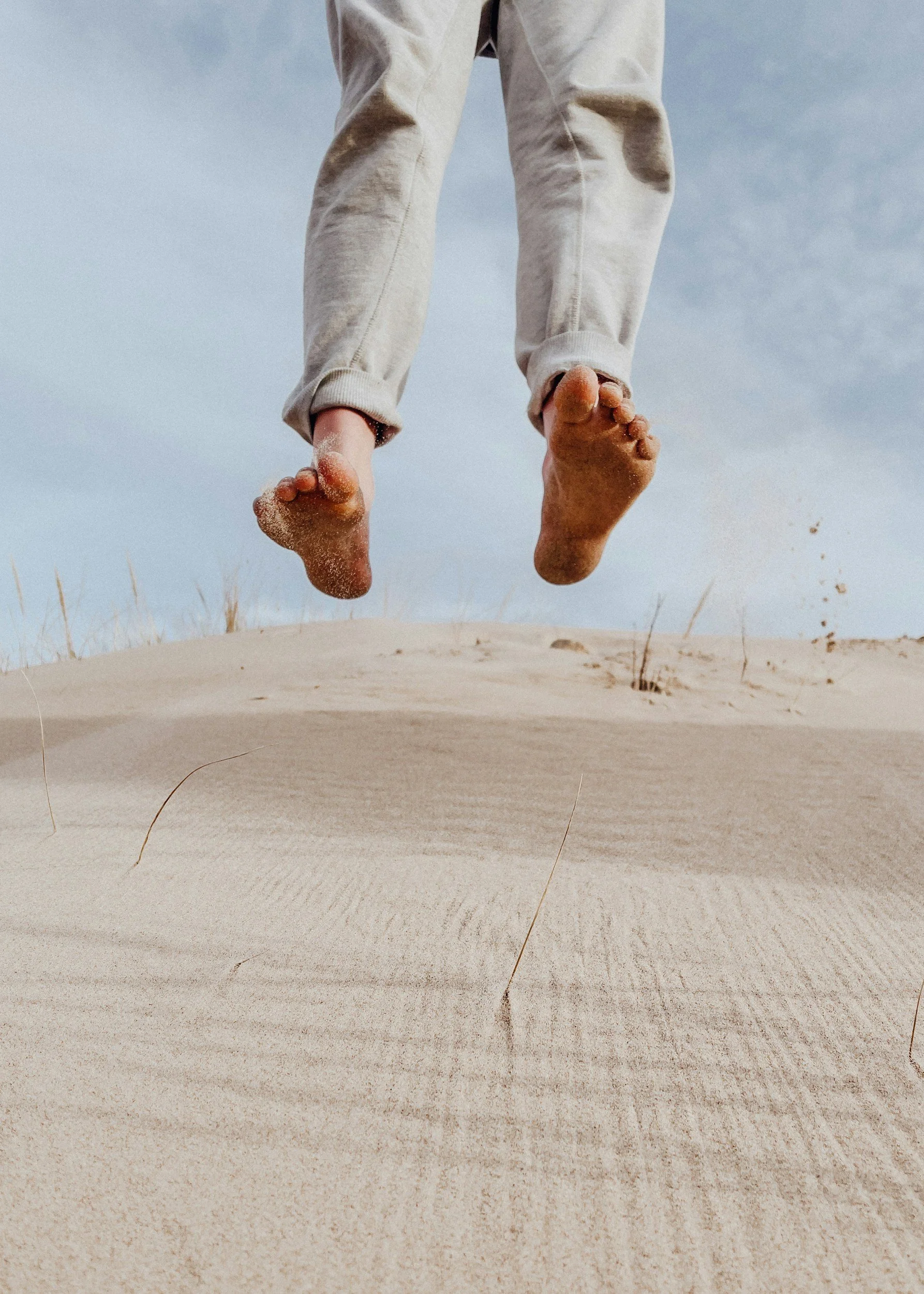 Two feet of a person who has jumped out of the frame in a sandy location..