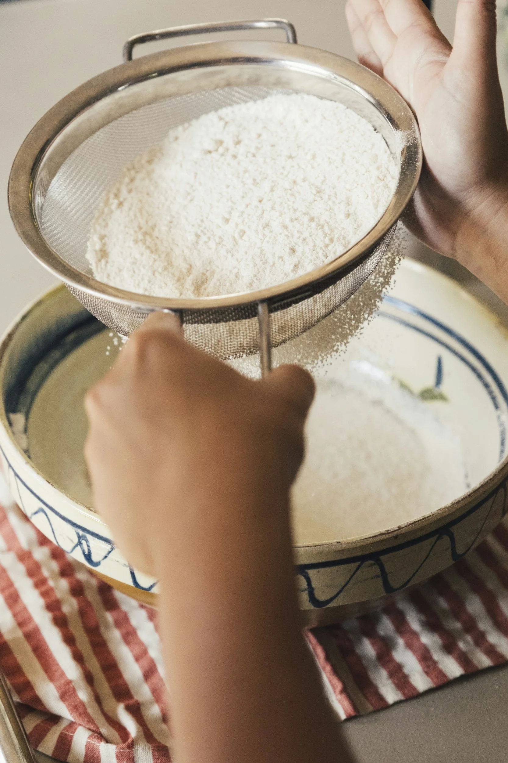 Hands sifting flour into a mixing bowl