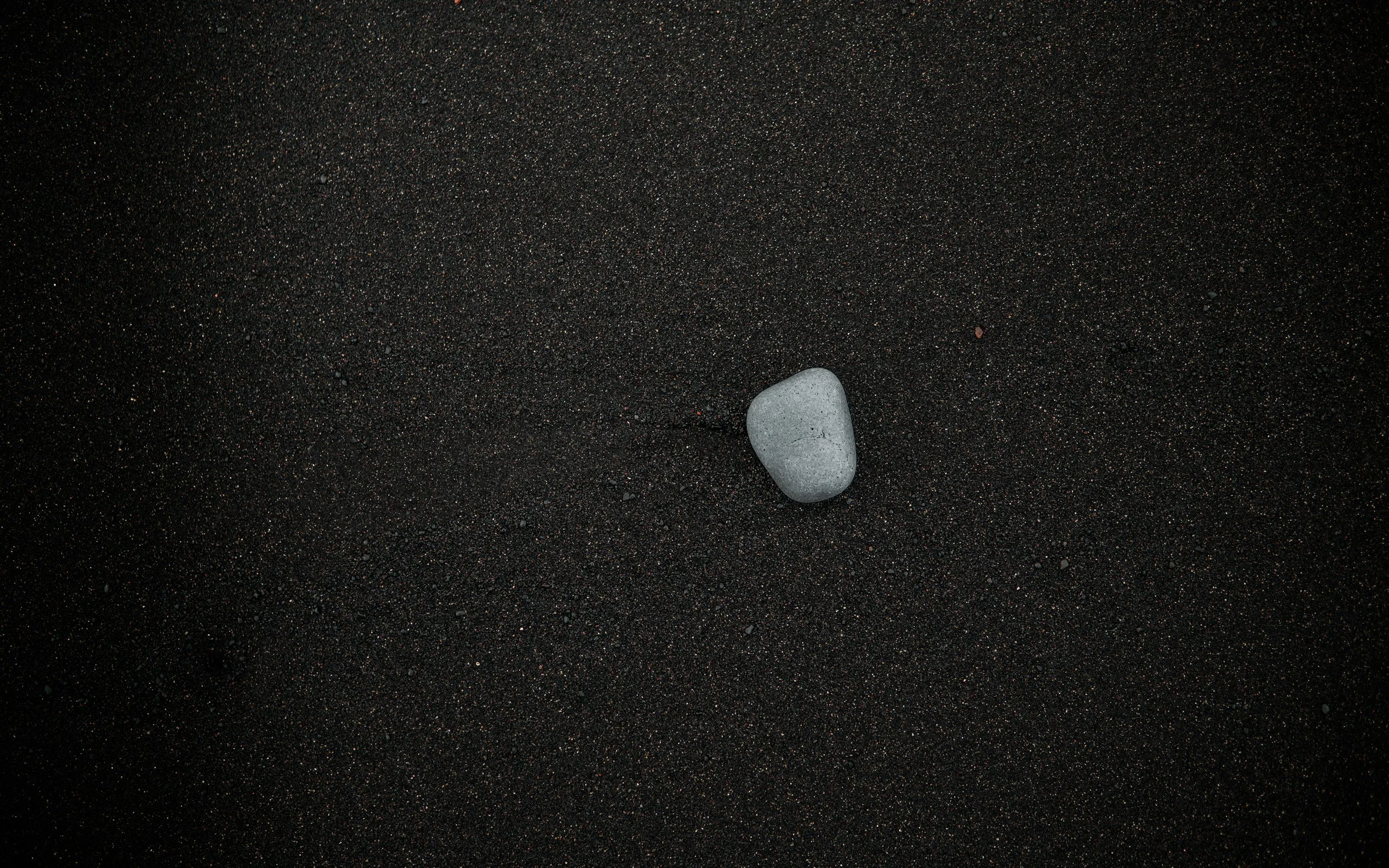Photo of a gray rock sitting on a black sandy beach