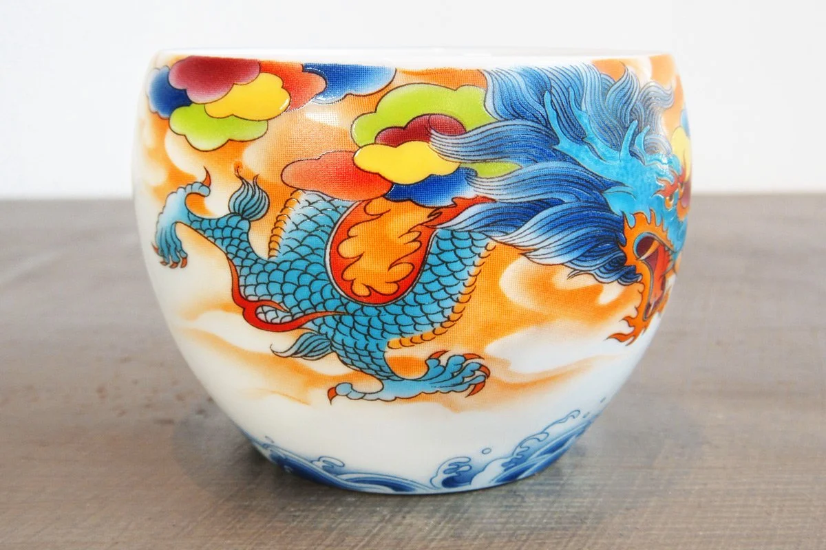 Closeup of a teacup with a blue dragon on a background of colorful clouds