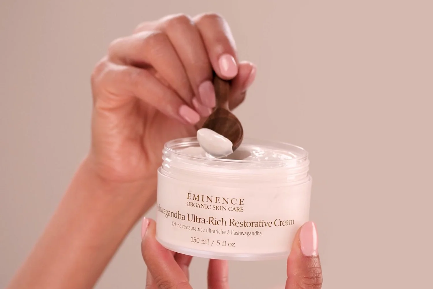 A woman using a small wooden spoon to scoop out the Ashwagandha Ultra-Rich Restorative Cream