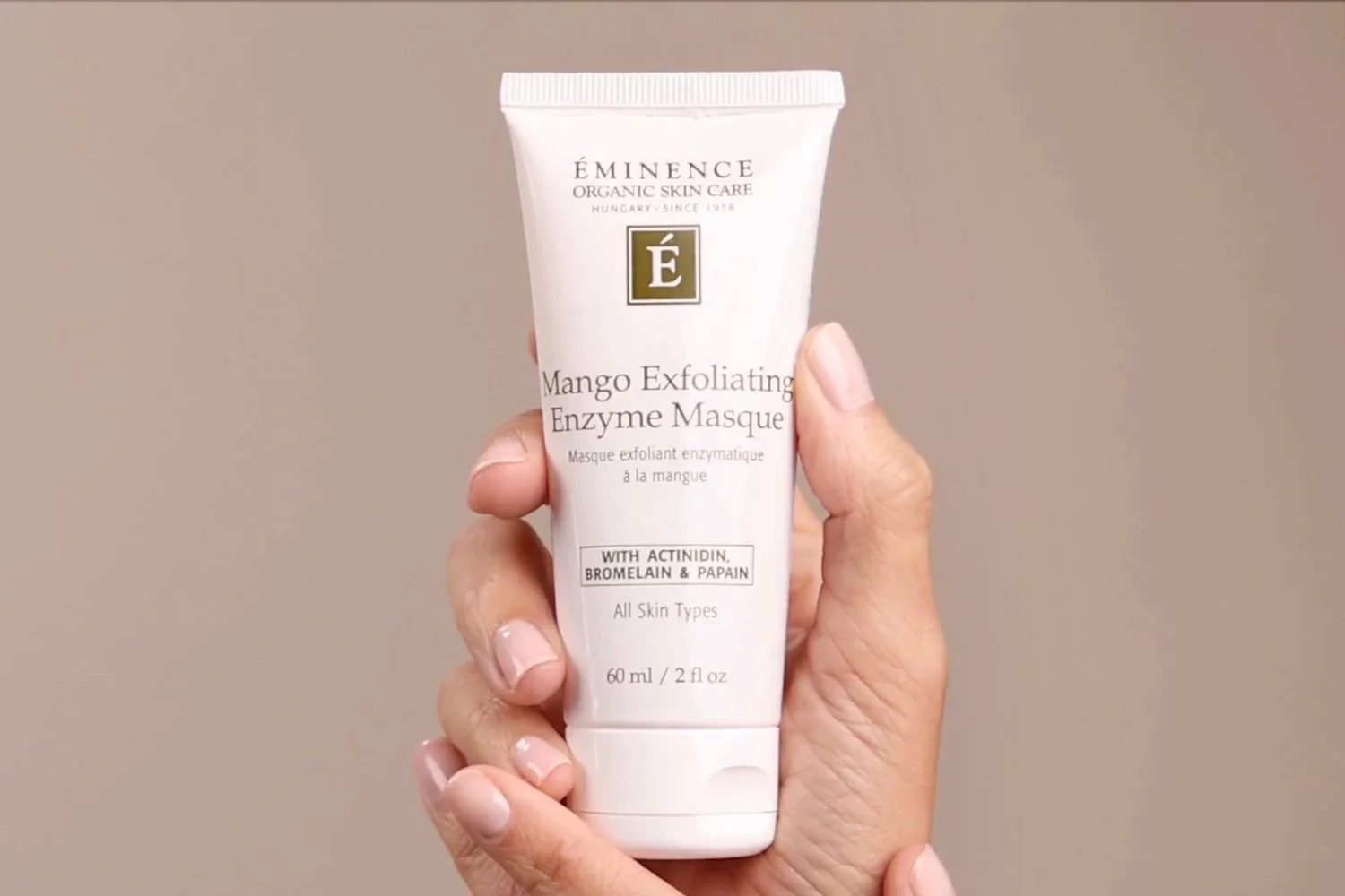 A hand holding the Eminence Organics Mango Exfoliating Enzyme Masque tube