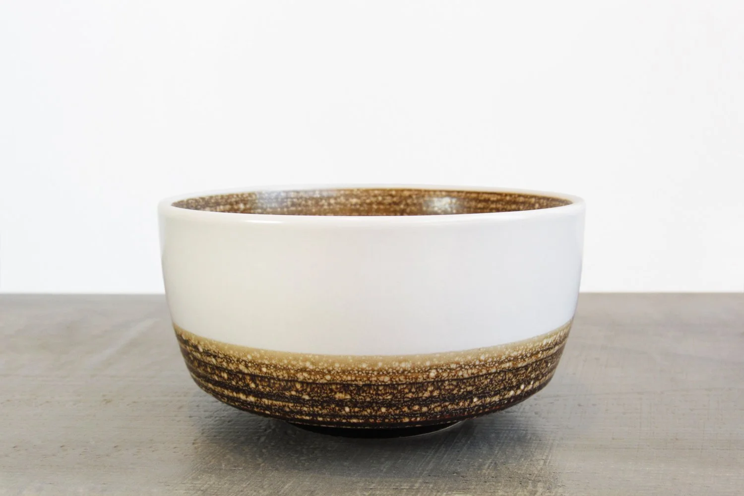 Creamy white and brown reactive glaze matcha bowl on a gray wood table