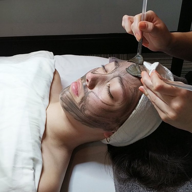 kincare esthetician applying a clay face mask on a woman’s face during a facial treatment