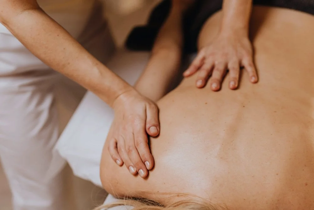 Massage therapist using light touch to gently massage a client’s back during a lymphatic drainage treatment
