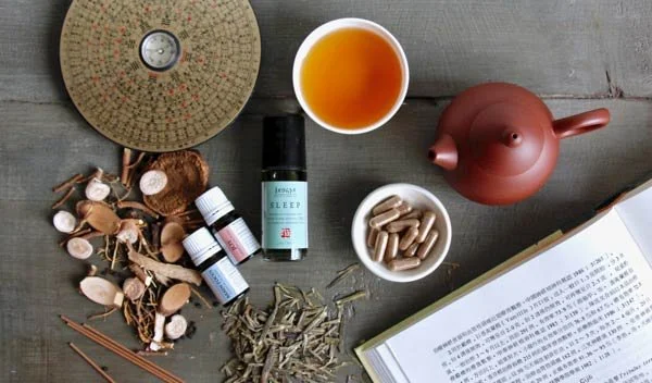 Traditional Chinese herbs, herbal supplements, and essential oil blends next to an open book on Chinese medicine