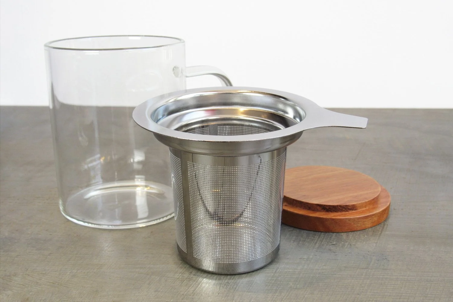 Extra-fine stainless steel infuser in front of glass mug and wooden teacup lid