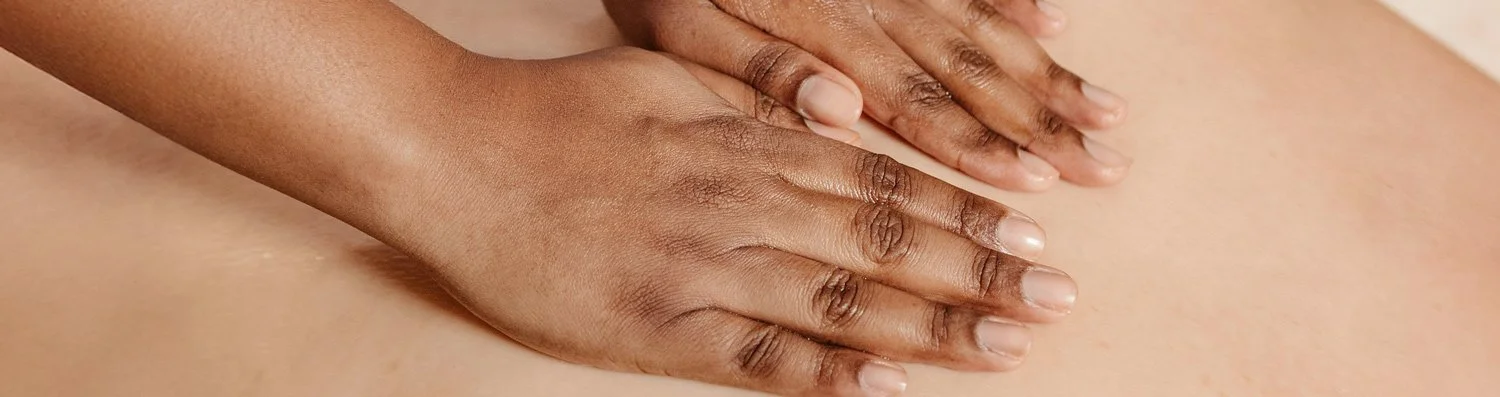 Close-up of a massage therapist gently resting their hands on a client’s back during an energy healing session