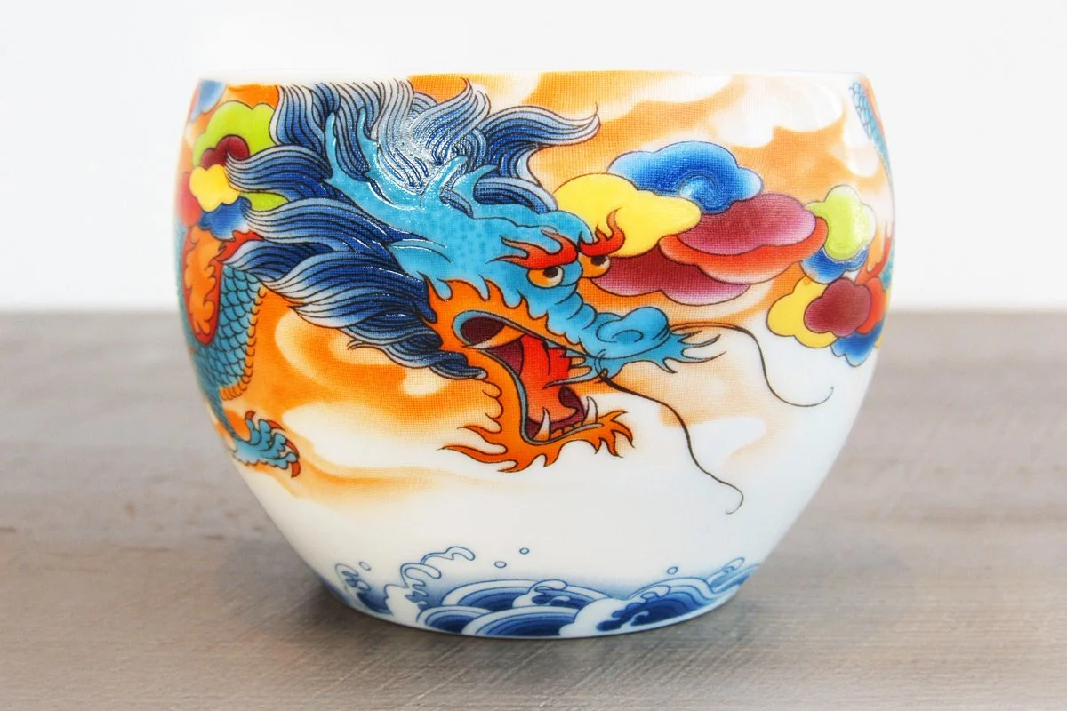 Closeup of a teacup with a blue dragon on a background of colorful clouds