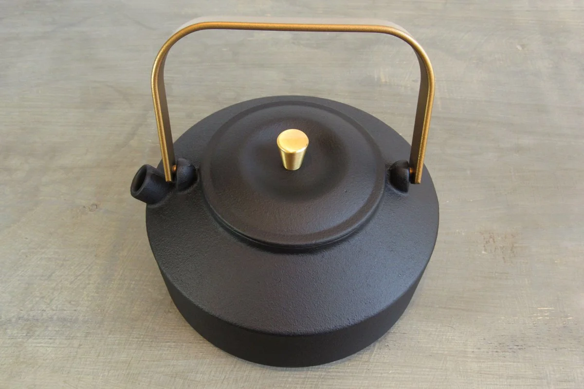 Matte black cast iron teapot with a textured exterior and a gold handle and teapot knob