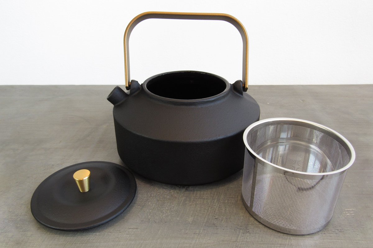 Black cast iron teapot with a gold handle and teapot knob and stainless steel infuser basket