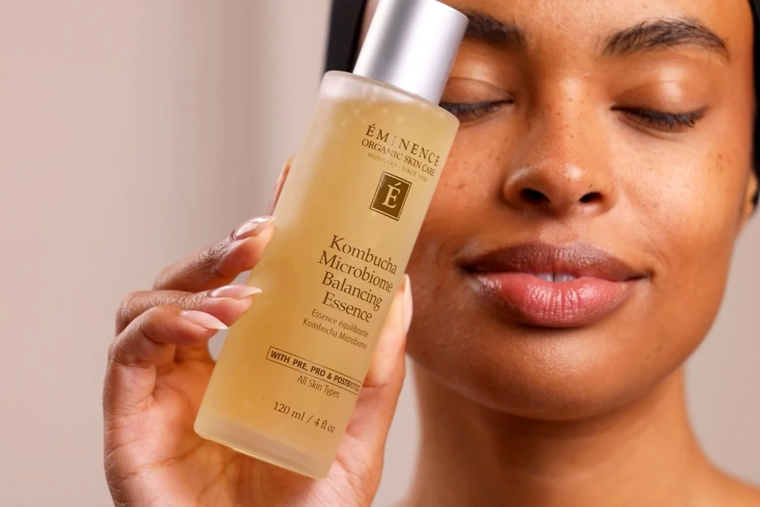A woman holding the Eminence Organics Kombucha Microbiome Balancing Essence glass bottle in front of her face