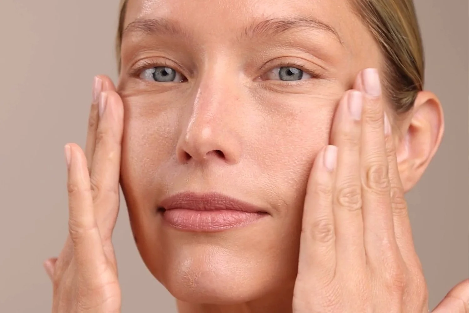 A close up of a woman applying the Eminence Organics Mango Exfoliating Enzyme Masque to their face