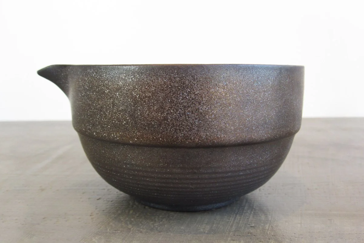 Side view of spouted matcha bowl with a dark textured glaze with a metallic shimmer