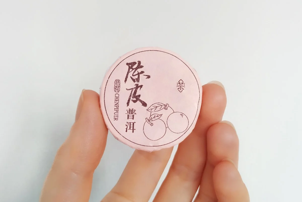 Hand holding one wrapped mini tangerine pu'er tea cake