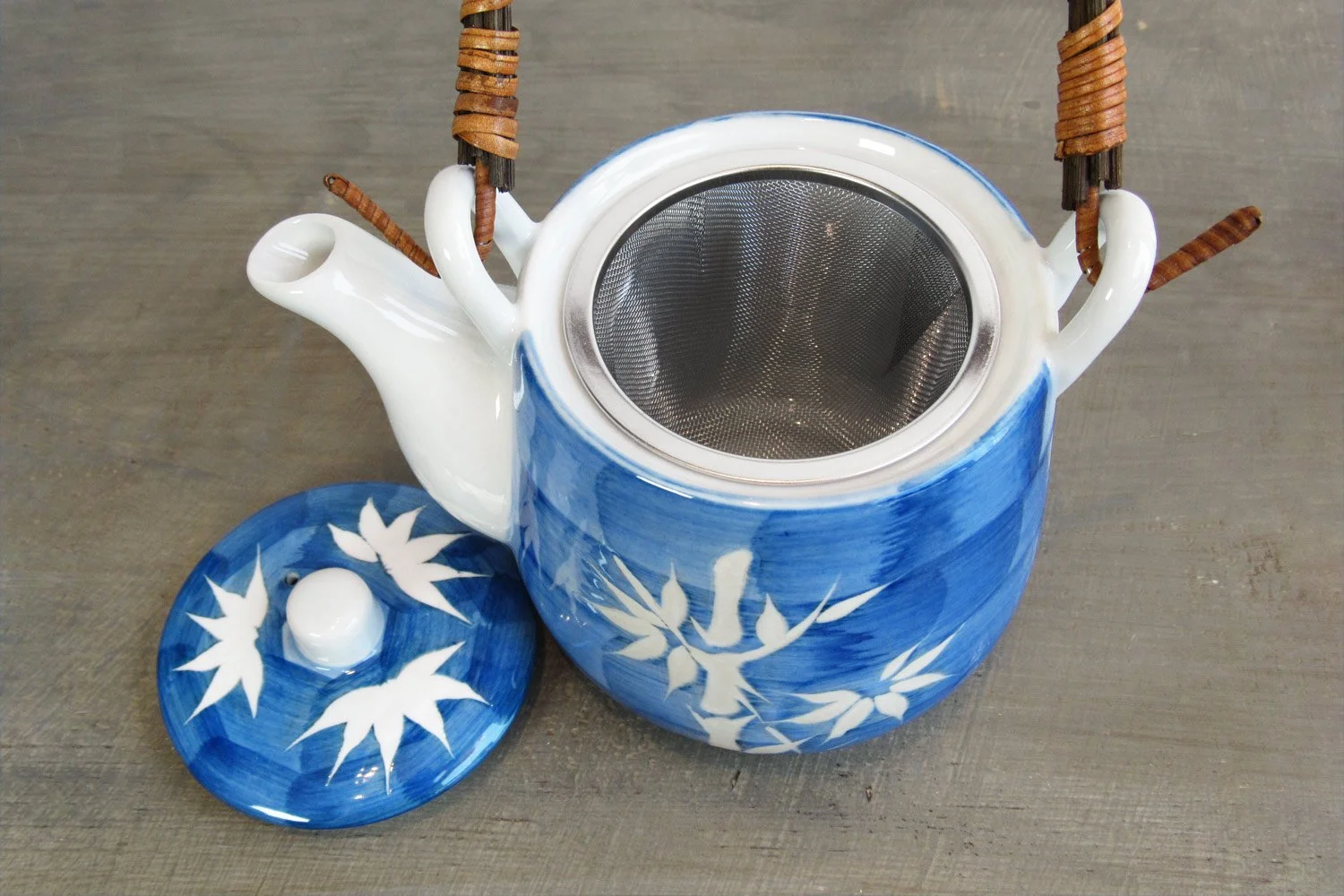 top-down view of a blue & white bamboo pattern teapot with a rattan handle and stainless steel strainer