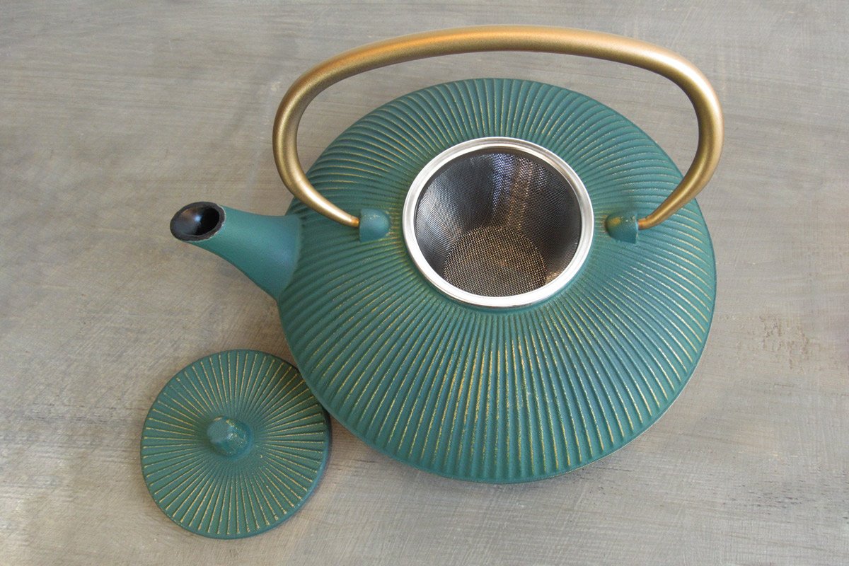 Top-down view of a teal cast iron teapot showing the stainless steel infuser basket inside