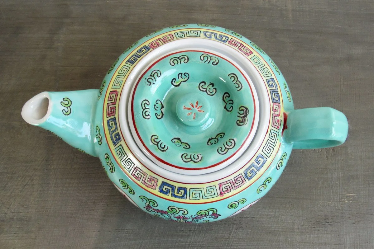 Top-down view of a turquoise teapot with hand-painted botanical patterns