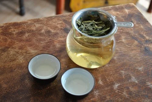green tea leaves steeping in a strainer and two tea cups of tea