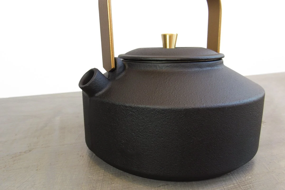 Matte black cast iron teapot with a textured exterior and gold handle
