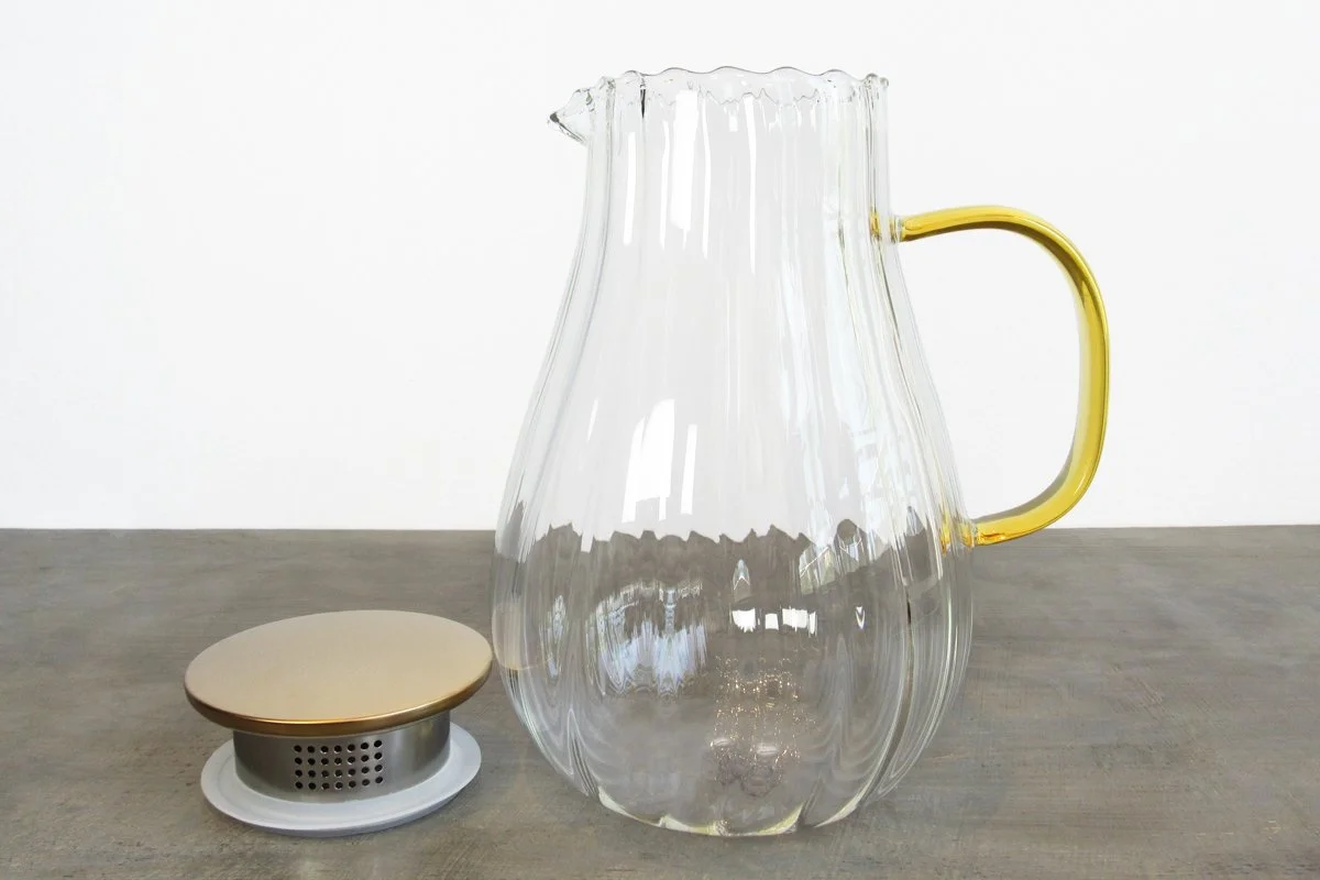Glass tea pitcher with a yellow handle next to the removable lid