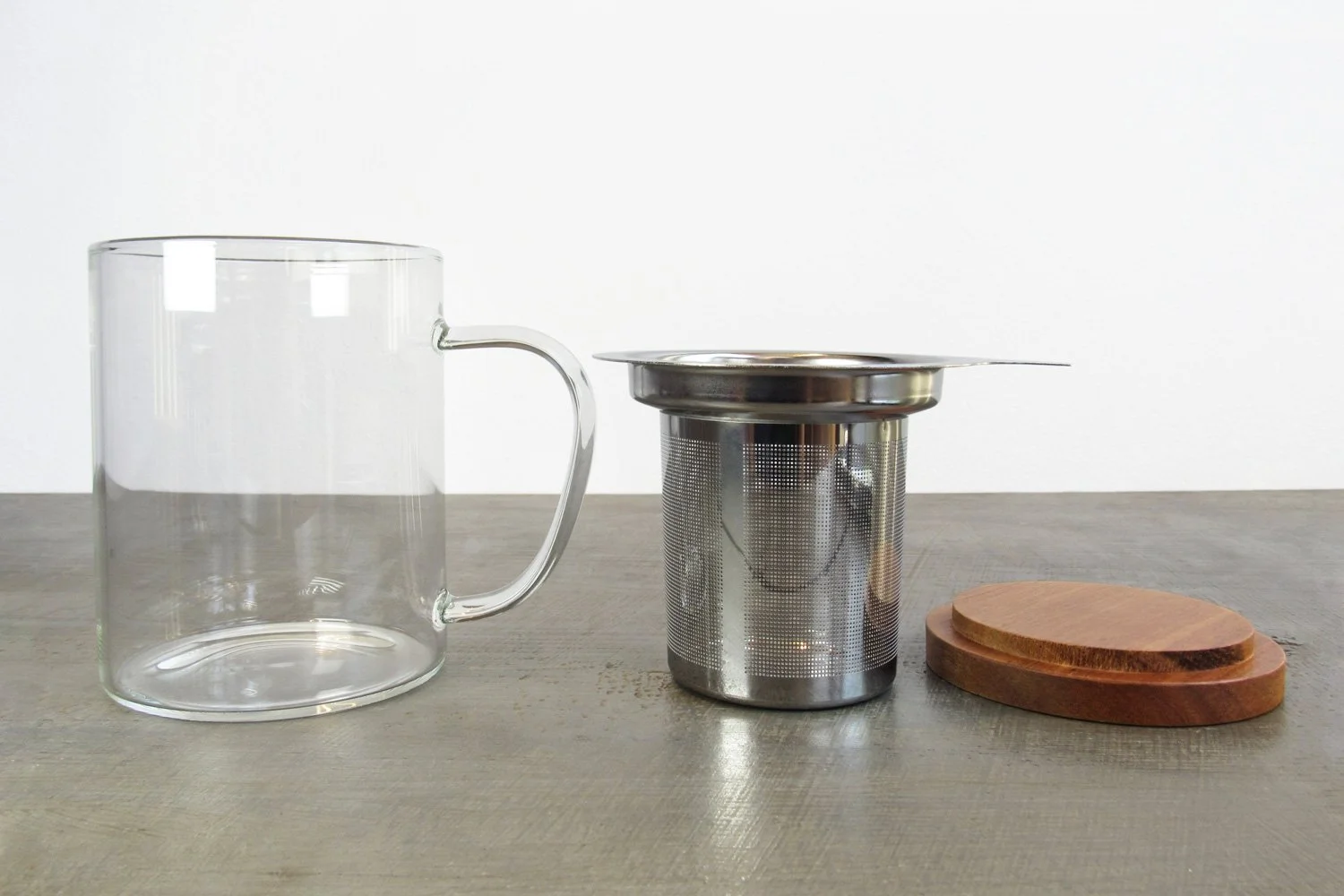 Glass teacup next to extra-fine stainless steel infuser and wooden lid
