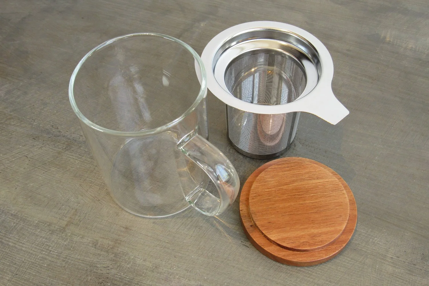 Glass teacup next to extra-fine stainless steel infuser and wooden lid