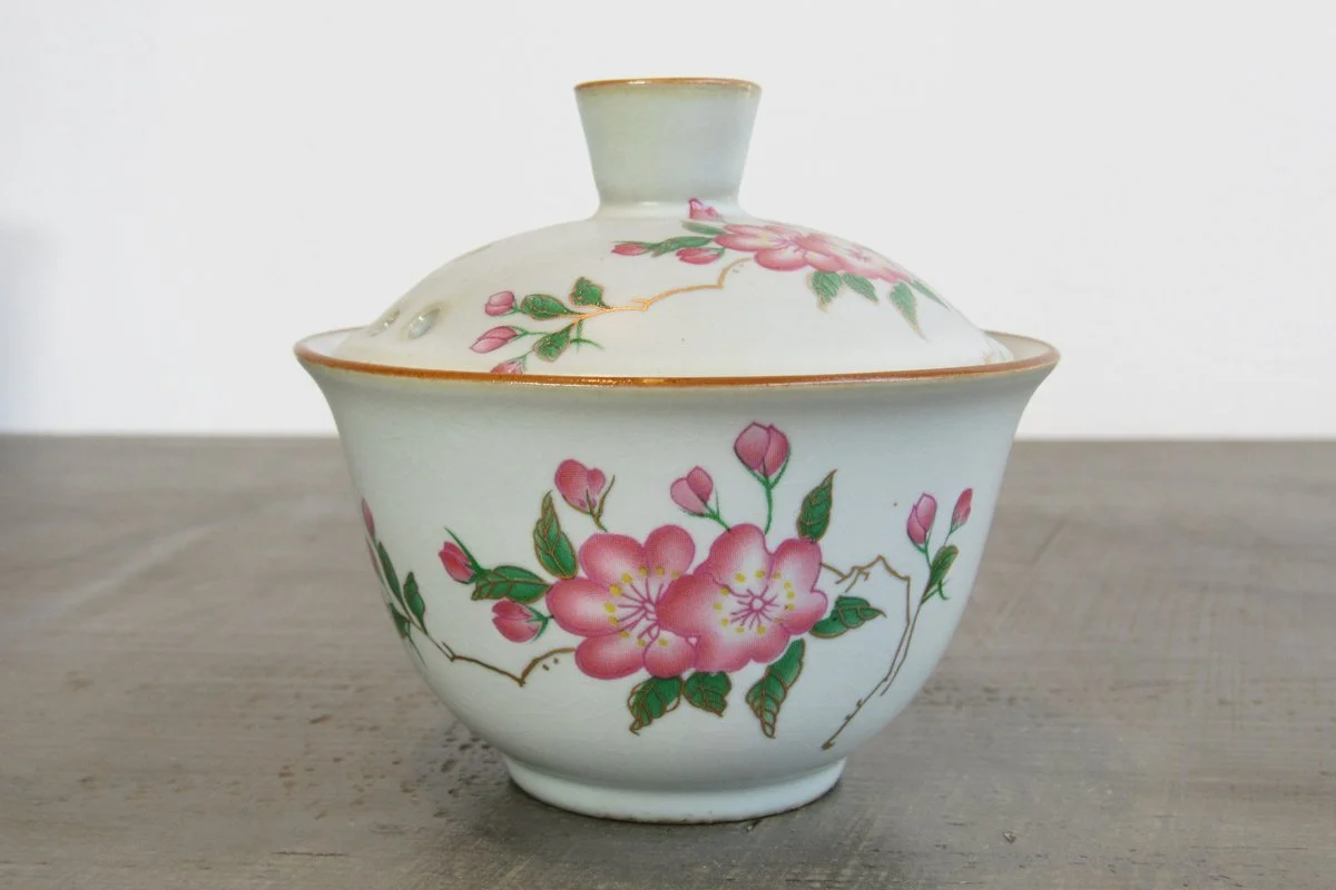 Close-up of a crackle glaze gaiwan adorned with pink blossoms, buds, and gold accents