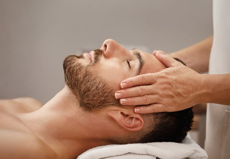 Esthetician resting their hands on a man’s face during a facial treatment