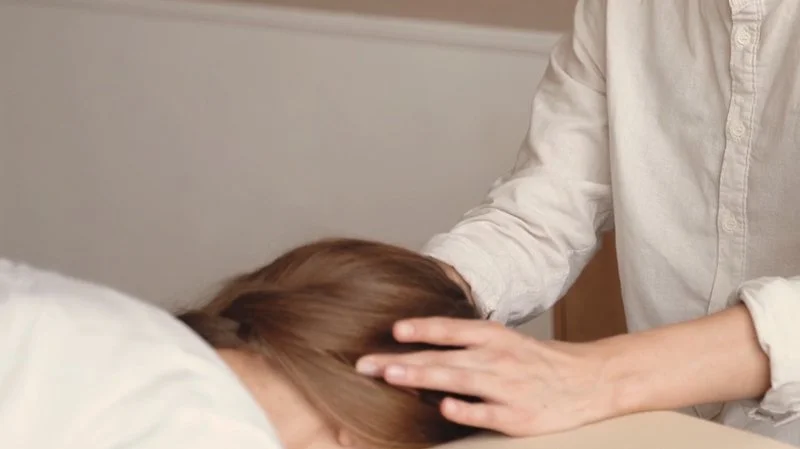 A practitioner with their hands gently placed on the head of a person lying face down