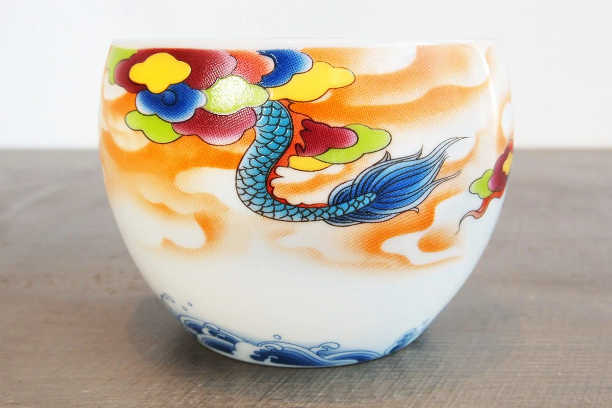 Closeup of a teacup with a blue dragon on a background of colorful clouds