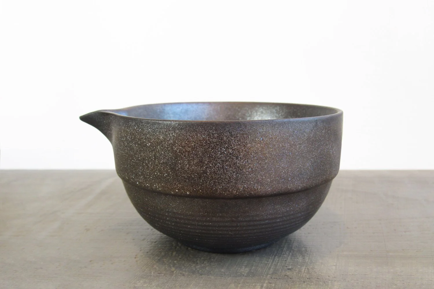 Dark-glazed matte matcha bowl with a metallic bronze sheen and pouring spout