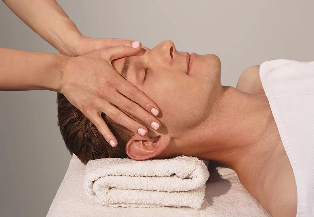 A man receiving a facial massage. An esthetician is gently pressing both hands on their forehead