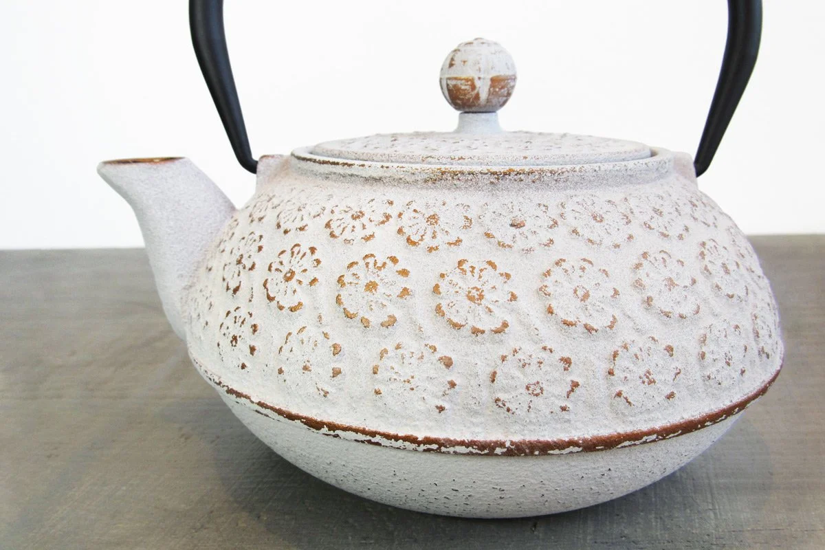 Closeup of a white cast iron teapot with a rustic finish and raised flower design