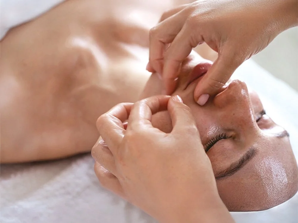 Esthetician using their fingers to massage a client’s lips and cheeks during a buccal massage