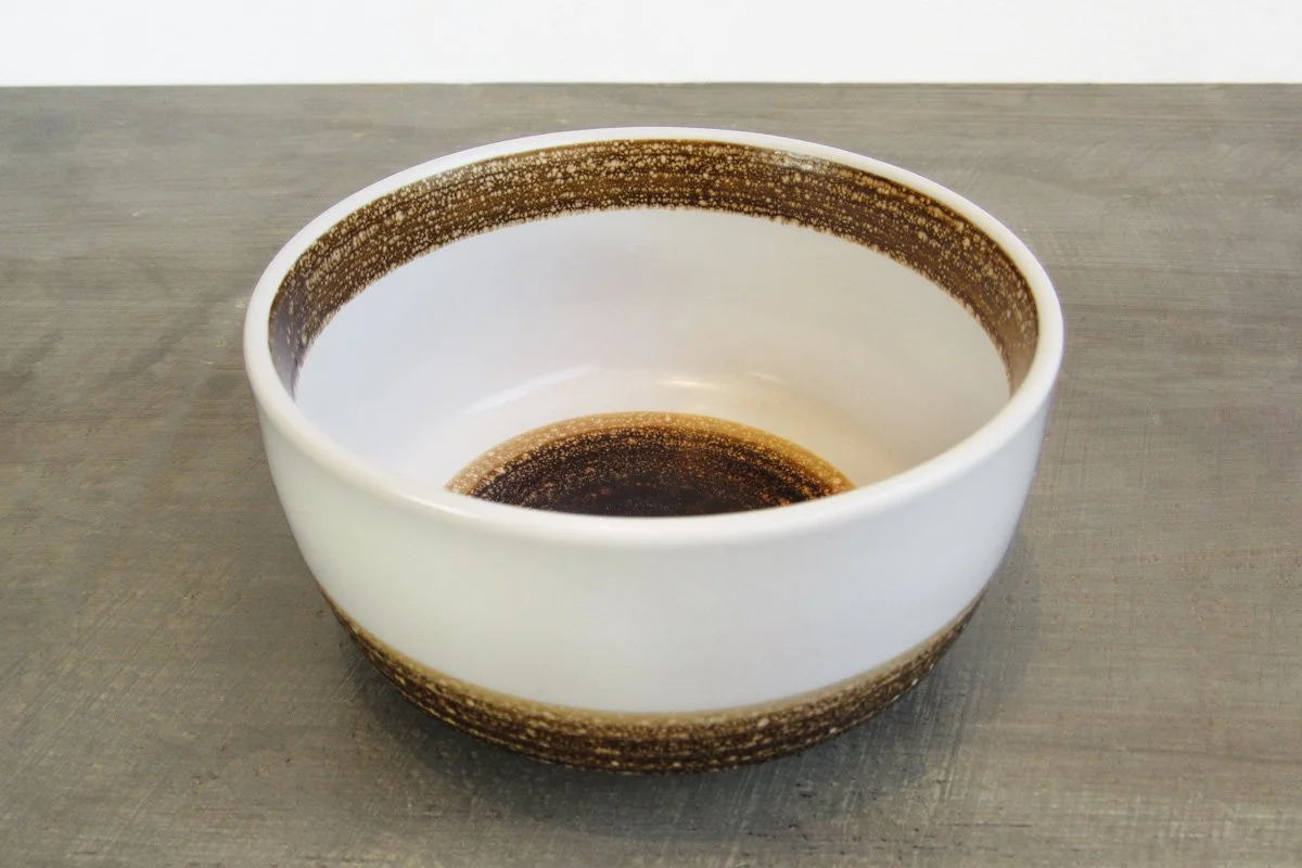 Side view of a white and brown glazed matcha bowl on a wood table
