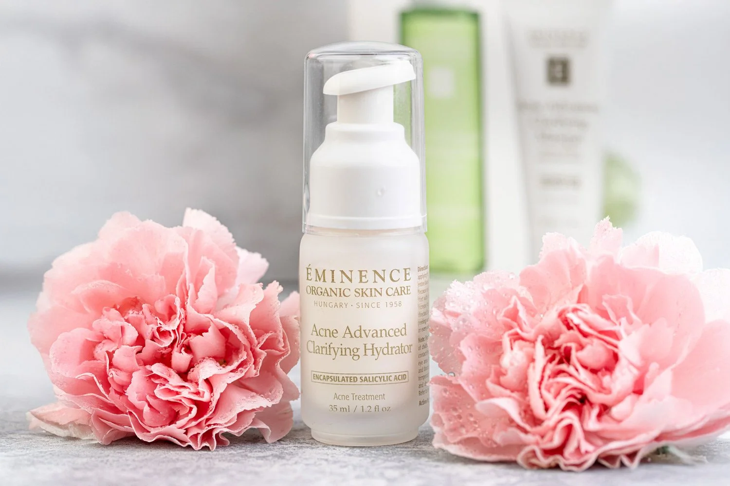 Eminence Organics Acne Advanced Clarifying Hydrator surrounded by pink flowers